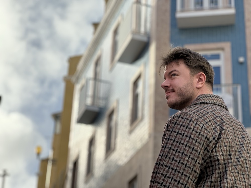 Ronny outdoors, looking up past pastel apartment buildings