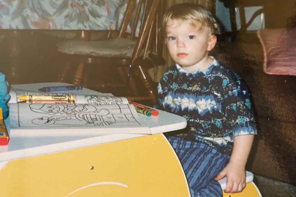 Ronny as a toddler at a small desk, coloring with crayons
